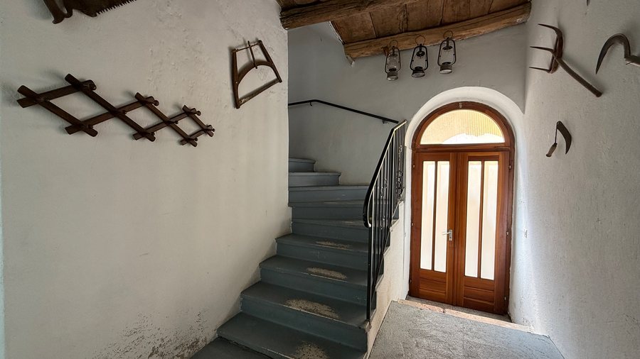 Ingresso storico con portone ad arco, scala e attrezzi d'epoca alle pareti