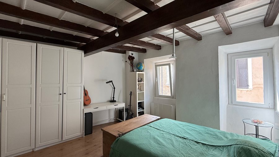 Camera matrimoniale con travi scure a vista, armadio bianco e pavimento in legno