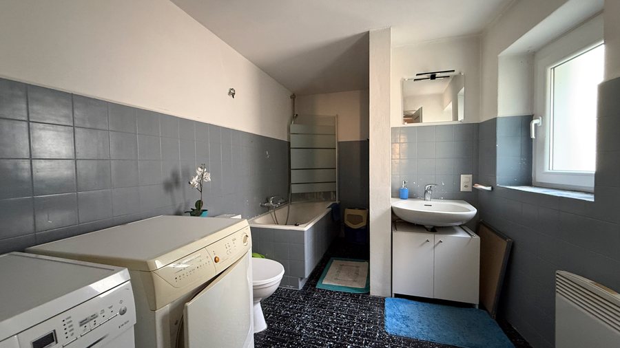Bagno grigio con vasca, lavabo e zona lavanderia collegato alla camera studio