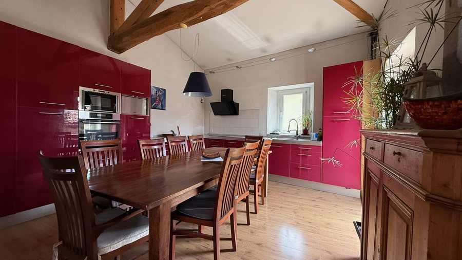 Cucina abitabile rossa con grande tavolo in legno e travi a vista